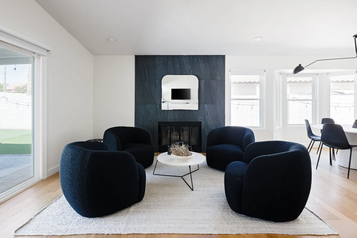 This image features a modern living room with four plush chairs arranged around a coffee table, a prominent fireplace, and a wall-mounted TV. The space is designed for socializing and relaxing, with a comfortable and contemporary feel that encourages conversation or cozy evenings by the fire.