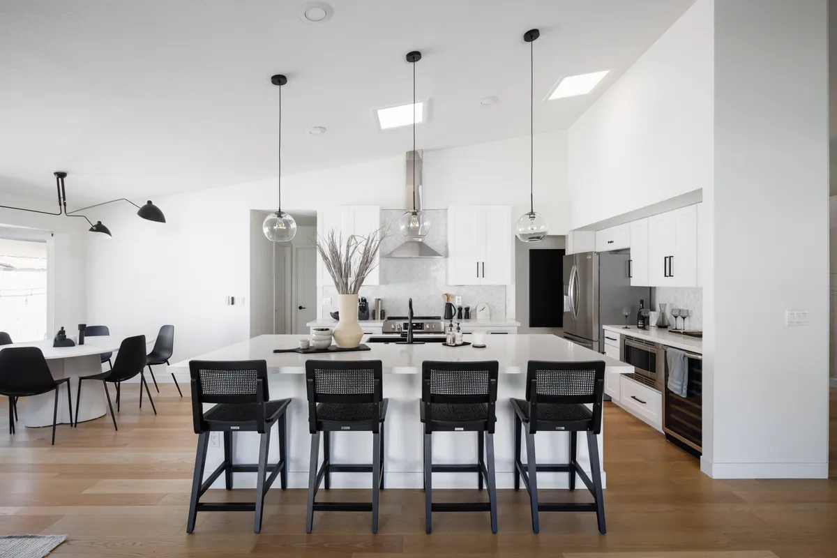 A contemporary kitchen scene showcases a central island with pendant lights, stainless steel appliances, and an adjacent dining table. The open-concept design highlights the seamless flow between cooking, dining, and socializing areas, reflecting a welcoming and modern atmosphere.