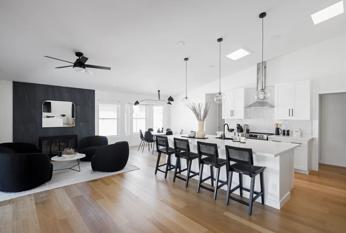 This interior view blends a kitchen island with bar stools, a cozy fireplace, large windows letting in natural light, and decorative elements for a stylish finish. The space is designed for both casual dining and intimate gatherings, with the fireplace adding a touch of warmth and ambiance.