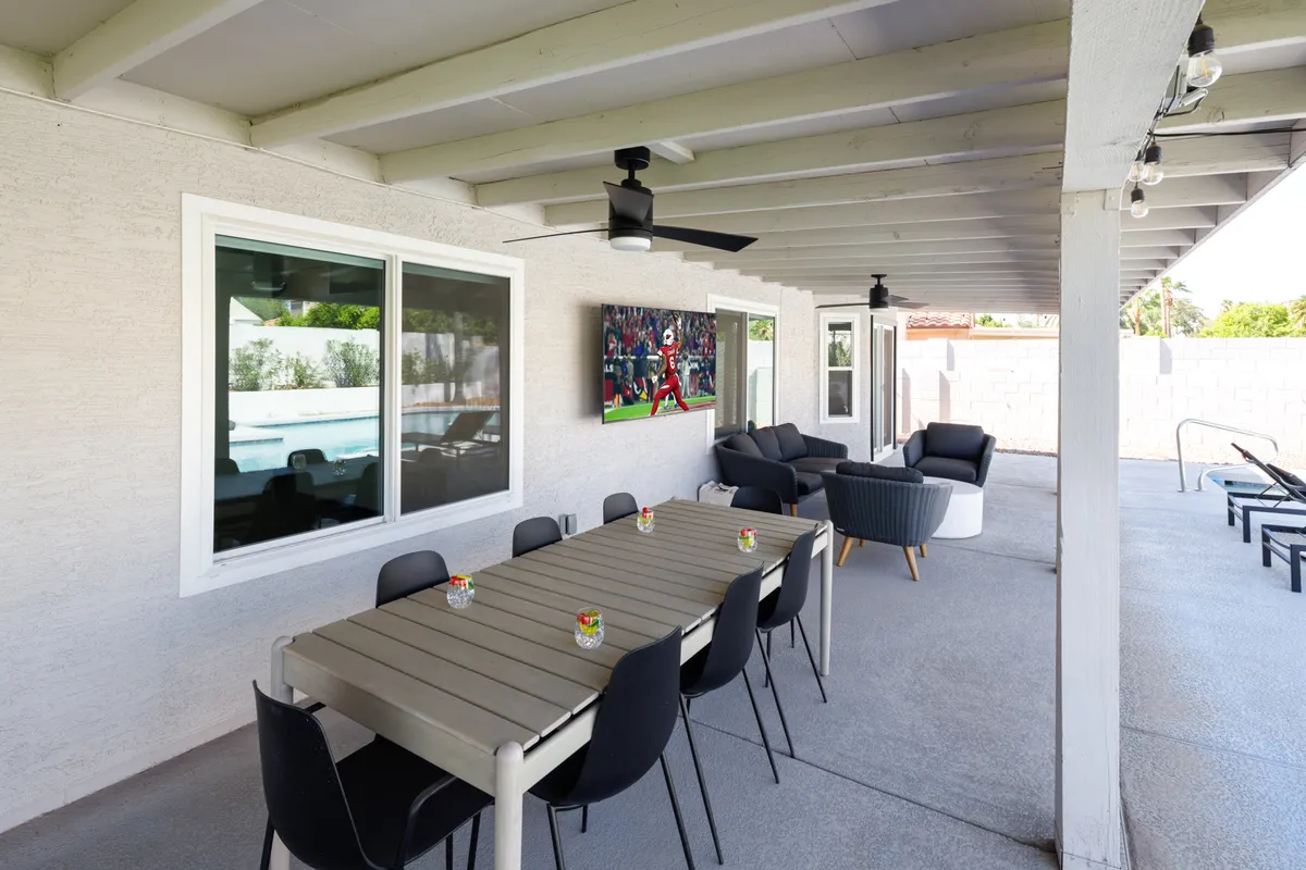 A sophisticated outdoor dining and lounge area with a long dining table, plush seating, and an outdoor television, all set for al fresco meals and entertainment. The space is designed for both relaxation and lively gatherings, seamlessly extending the living area outdoors.