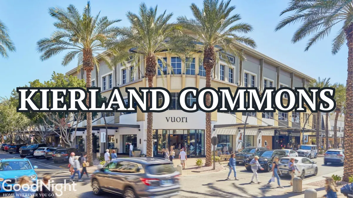 A lively streetscape scene with the building facade, palm trees, and visible shop signage. The street bustles with people shopping and dining, capturing the vibrant, upmarket energy of local attractions like Kierland Commons.
