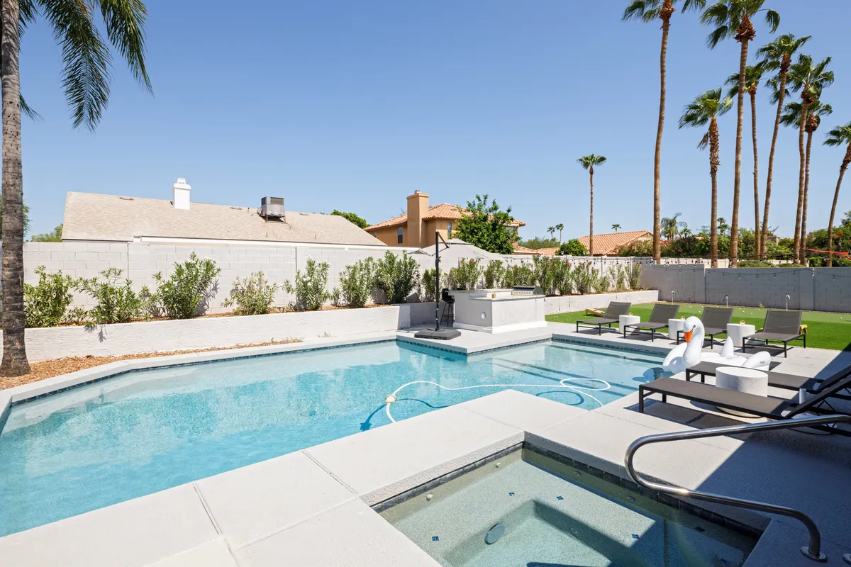 A vibrant backyard setting featuring a swimming pool, hot tub, lounge chairs, palm trees, and an outdoor kitchen. This space is designed for relaxation and entertaining after a day on the golf course.