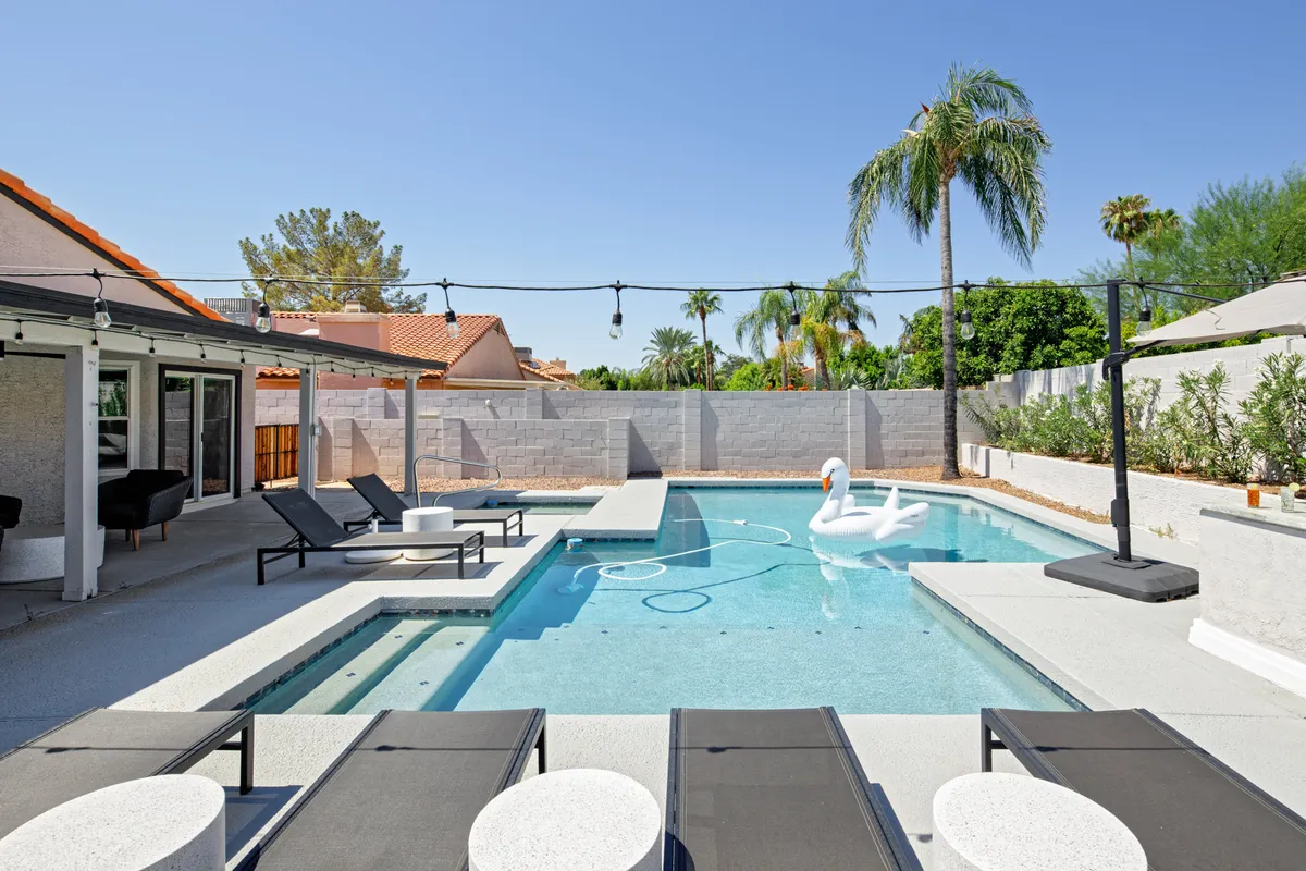 This inviting exterior shot features a sparkling swimming pool surrounded by lounge chairs, a whimsical swan float, and soft string lights hung above. The setting is playful yet serene, suggesting opportunities for relaxation and intimate evening swims or sunbathing.