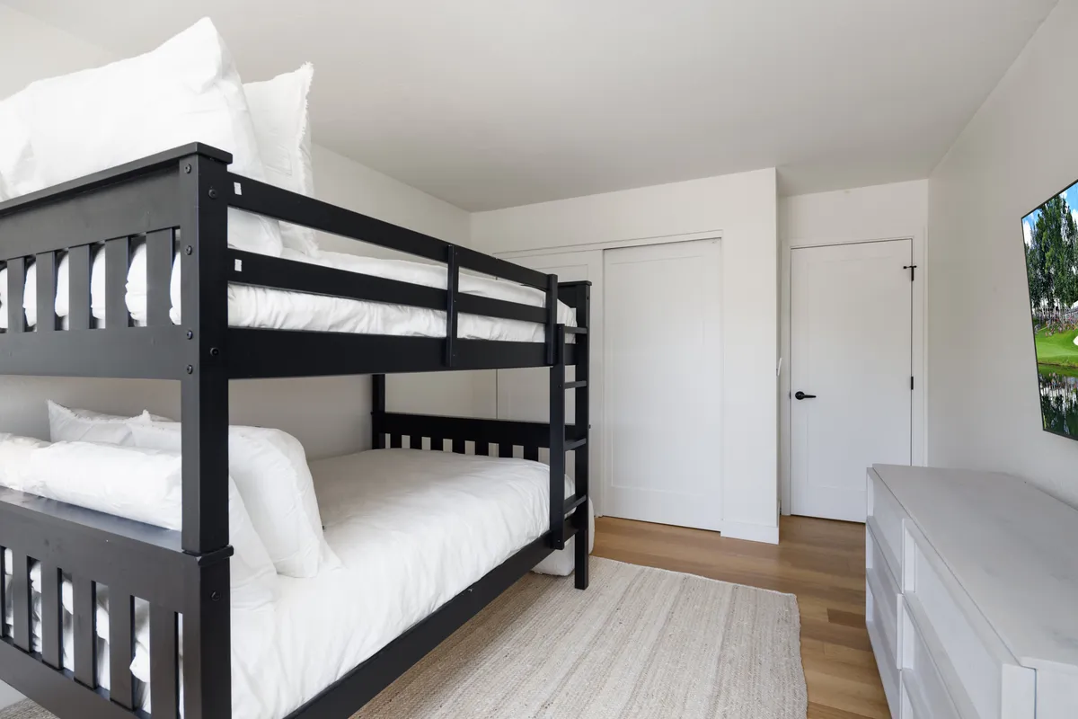 A playful and cozy bedroom with full-sized bunk beds, a white dresser, and a large wall-mounted TV. The youthful decor and layout make it perfect for kids or extra guests, offering both comfort and in-room entertainment. The space feels inviting and adaptable for groups or families.